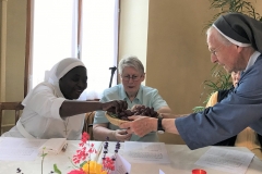 Sr Chantal tendue vers Sr Marie-Chantal pour offrir un grain de raisin