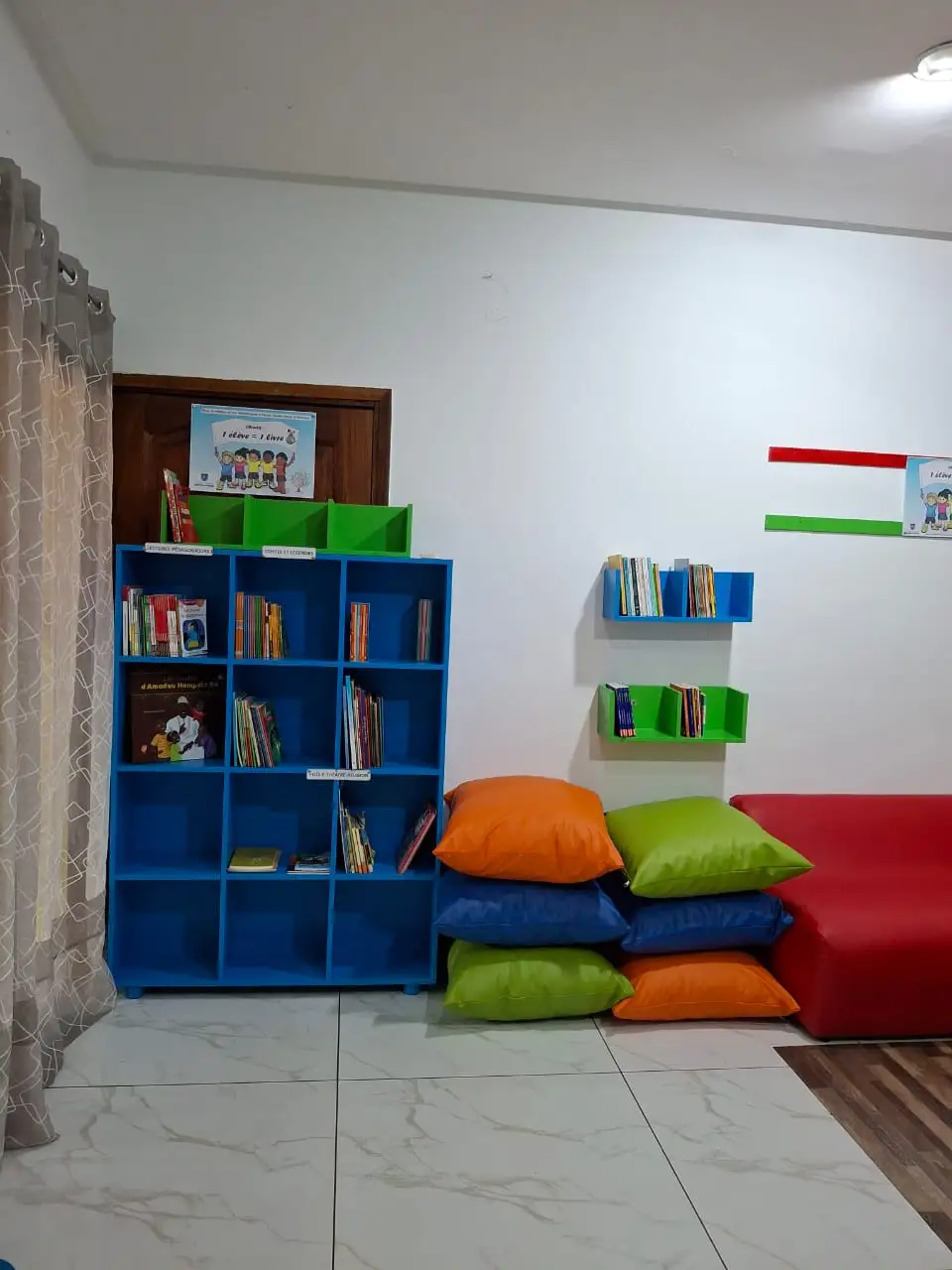 A blue bookcase with books, wall shelves and colourful cushions next to a red sofa