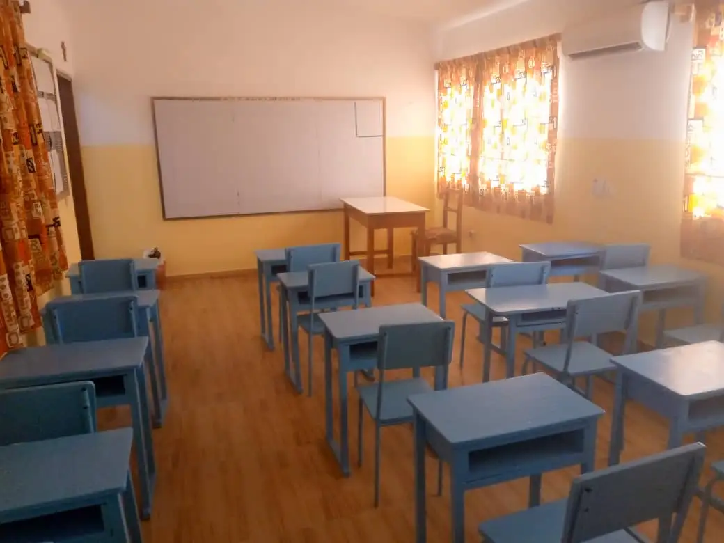 Une salle de classe de l’école, pupitres bleus alignés face au tableau blanc