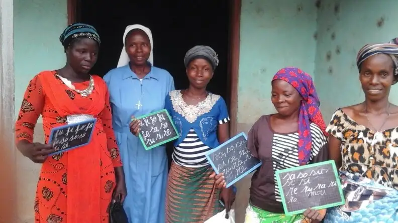 Des femmes tenant chacune une ardoise devant une maison, avec une sœur