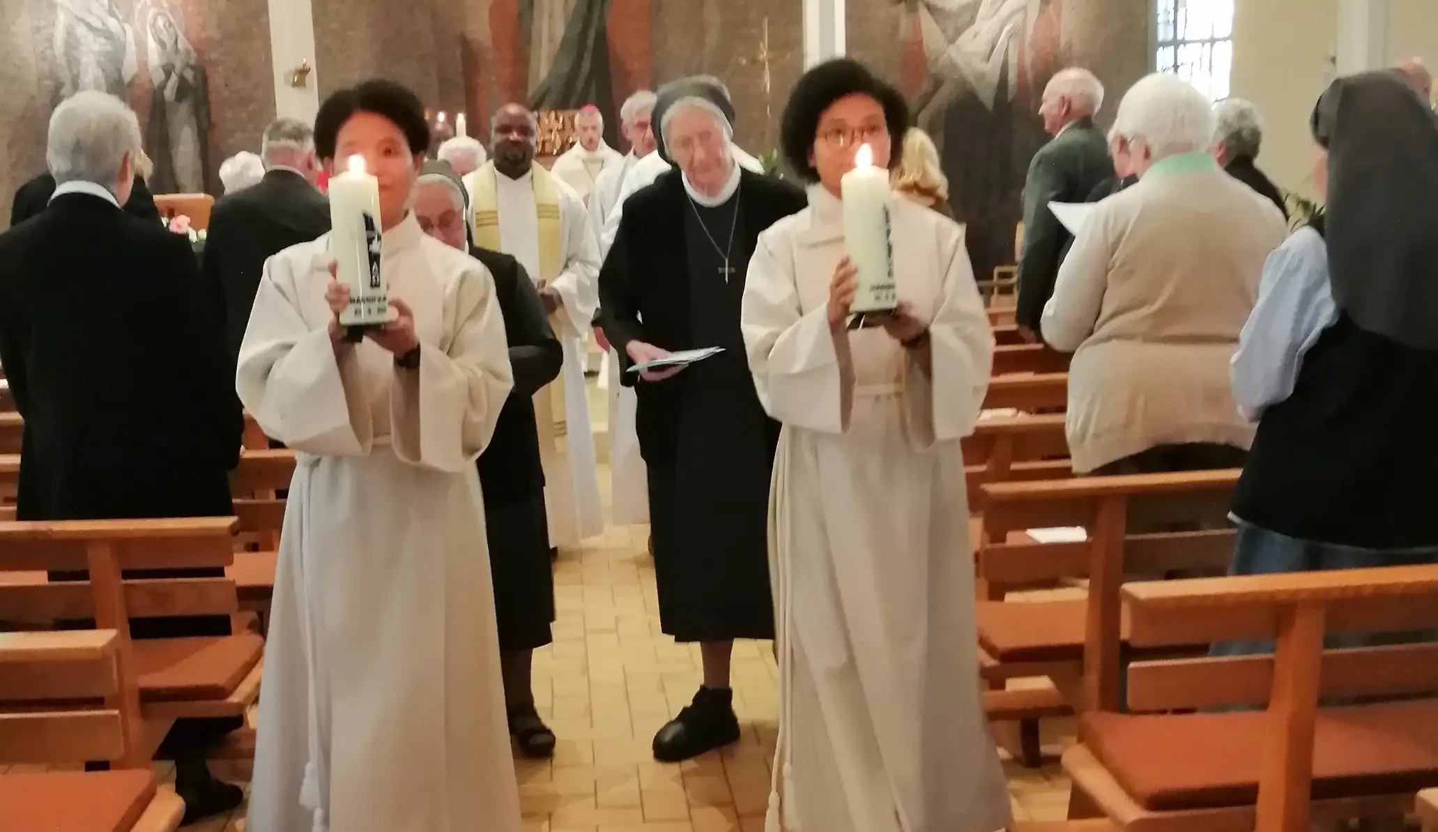 Deux jeunes femmes portent les cierges dans la chapelle de la Maison-Mère, en 2021